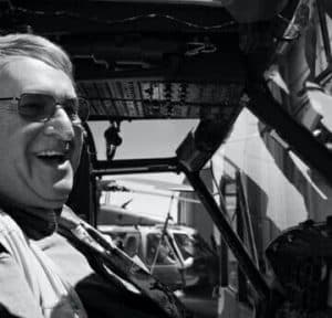 Older white man wearing glasses and smiling in a plane cockpit. 
