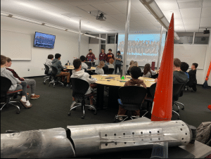 Group of young men give a presentation in a room of intersectional youth about rockets. 