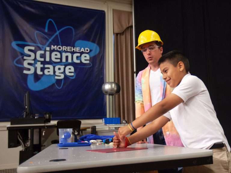 Man in a yellow hard had and a intersectional youth doing a science experiment.