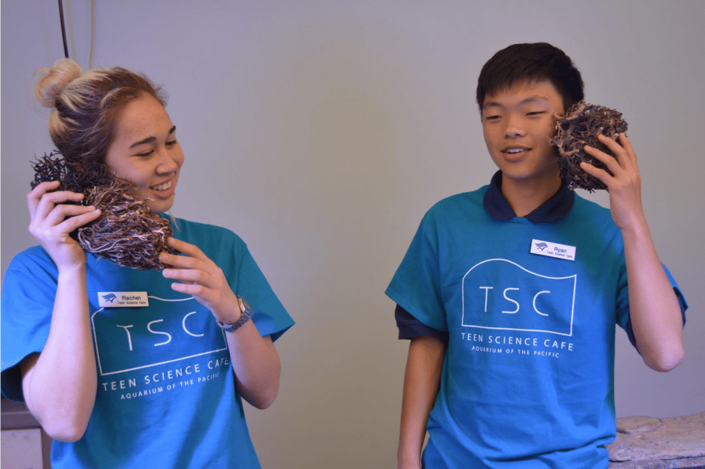 Two intersectional youth in matching blue t-shirts hold shells to their ears.