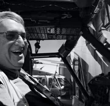 Older man wearing glasses and smiling in a plane cockpit.
