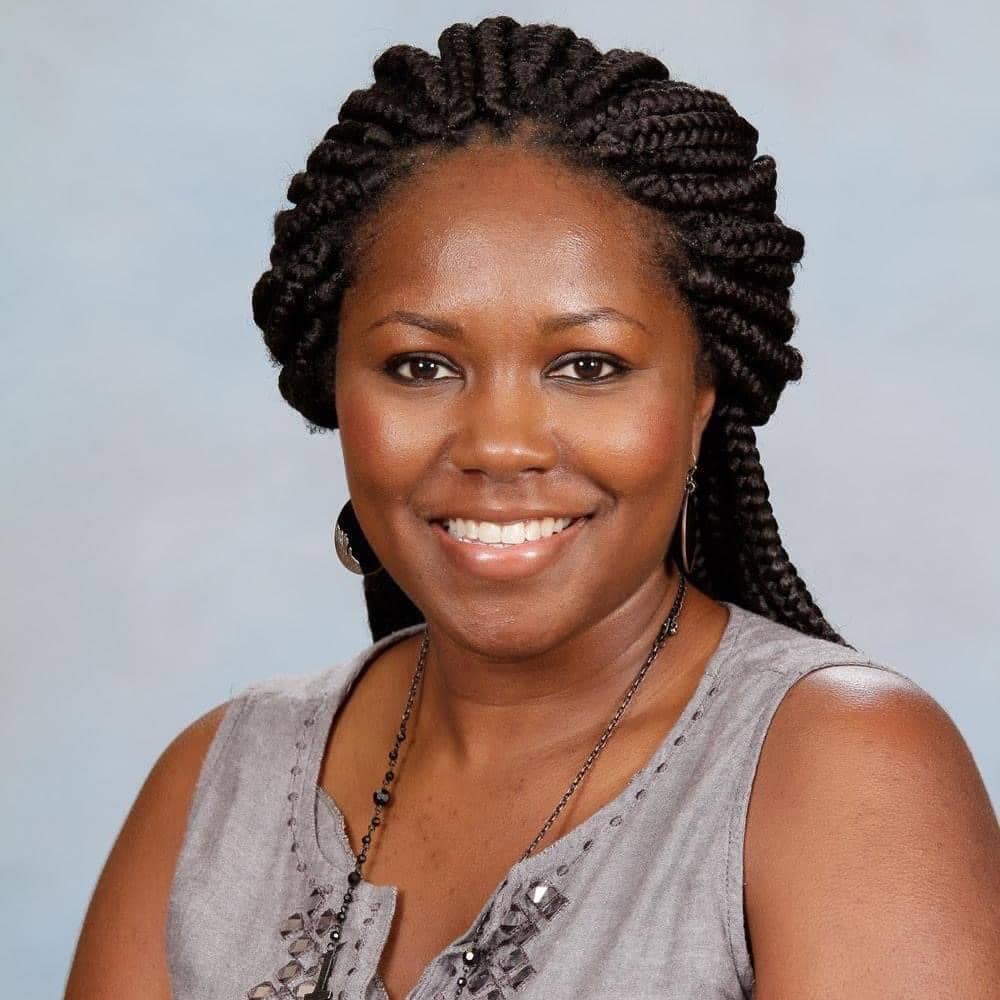 Portrait of an BIPOC woman with braids pulled back wearing a sleeveless brown top.